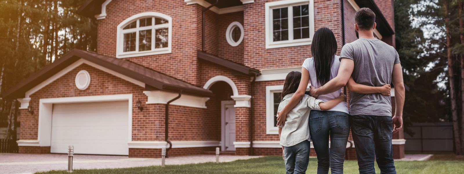 A family standing with their arms around each other facing their house.